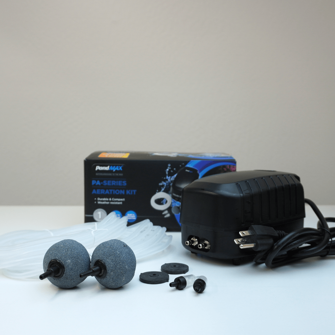 PondMAX PA14 aeration kit contents in front of its box: dual-outlet air pump, two 2-inch sphere air stones, two check valves, spare diaphragms and tubing